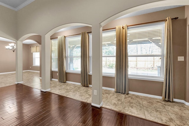 interior space with baseboards, arched walkways, wood finished floors, crown molding, and a chandelier