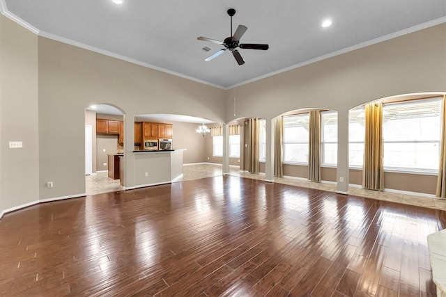 unfurnished living room featuring ceiling fan with notable chandelier, wood finished floors, and baseboards