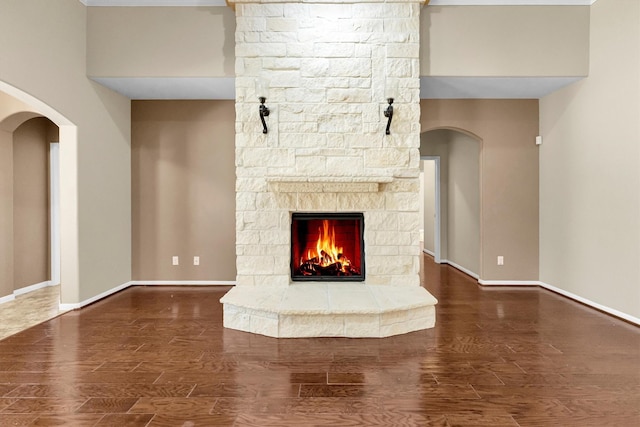 unfurnished living room with a stone fireplace, baseboards, and wood finished floors