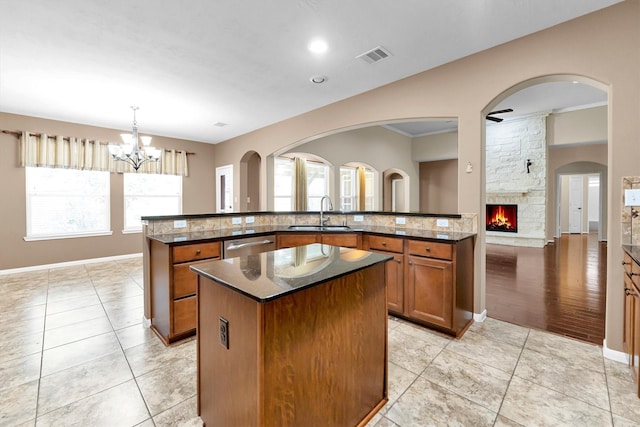 kitchen featuring light tile patterned floors, brown cabinets, a kitchen island with sink, a fireplace, and a sink