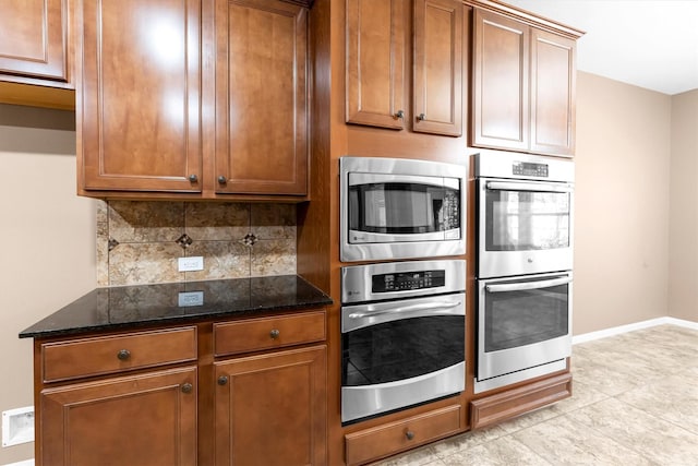 kitchen featuring dark stone counters, stainless steel appliances, brown cabinetry, and backsplash