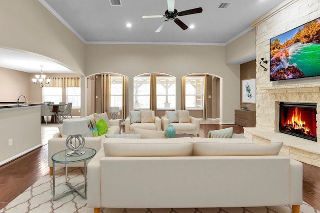 living area featuring arched walkways, crown molding, visible vents, a stone fireplace, and wood finished floors