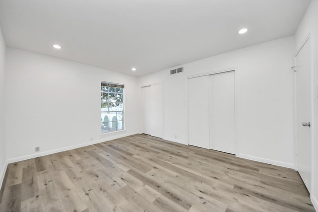 unfurnished bedroom with two closets, recessed lighting, visible vents, light wood-style flooring, and baseboards