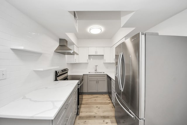 kitchen featuring light stone counters, appliances with stainless steel finishes, light wood-style floors, a sink, and wall chimney range hood