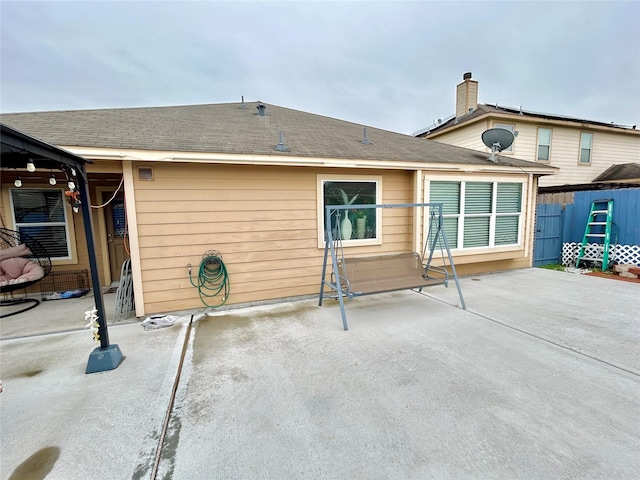 rear view of house with roof with shingles, a patio area, and fence