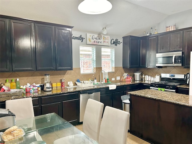 kitchen with stone countertops, decorative backsplash, vaulted ceiling, stainless steel appliances, and a sink