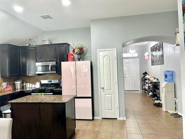 kitchen featuring arched walkways, stainless steel appliances, visible vents, light tile patterned flooring, and dark stone countertops