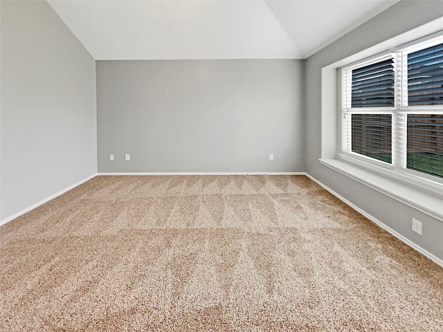 carpeted empty room featuring vaulted ceiling and baseboards