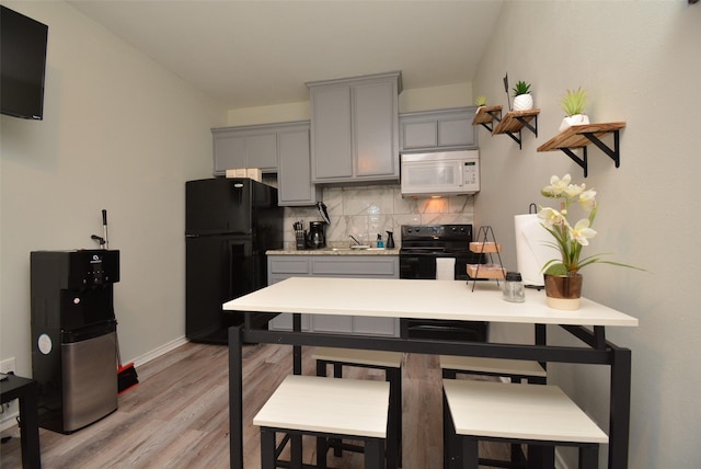 kitchen with a breakfast bar, gray cabinets, light countertops, backsplash, and black appliances