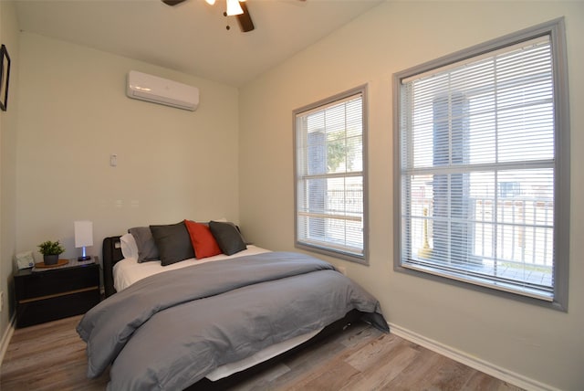 bedroom with ceiling fan, baseboards, wood finished floors, and a wall mounted air conditioner