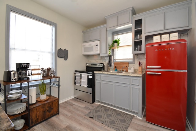 kitchen with white microwave, gray cabinetry, stainless steel electric stove, freestanding refrigerator, and decorative backsplash