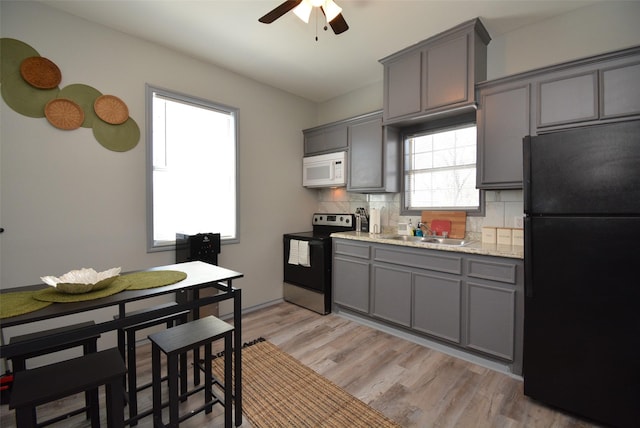 kitchen with white microwave, freestanding refrigerator, stainless steel electric stove, gray cabinets, and a sink