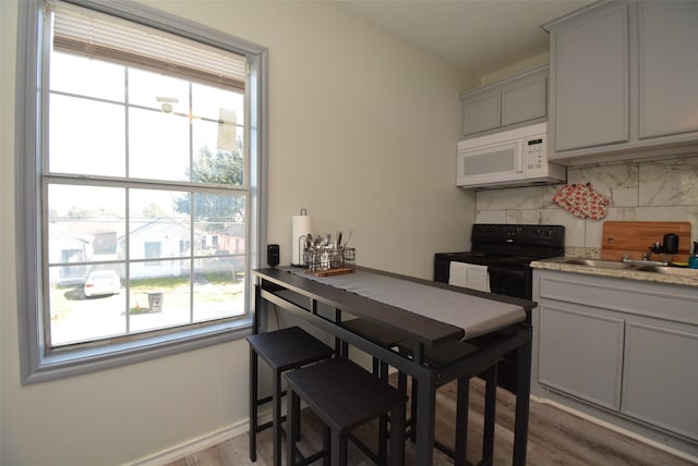 kitchen featuring backsplash, gray cabinetry, white microwave, wood finished floors, and black / electric stove