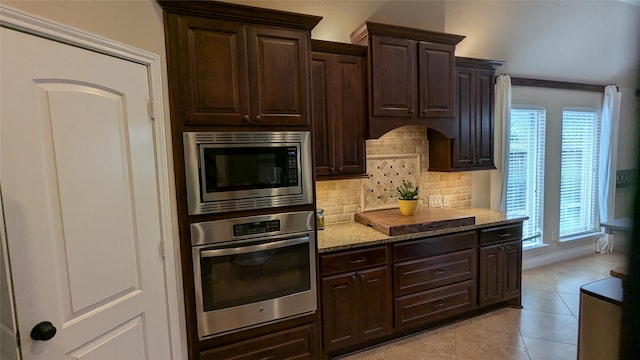 kitchen featuring tasteful backsplash, dark brown cabinets, light stone countertops, light tile patterned floors, and stainless steel appliances