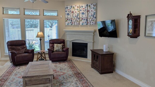 living area with baseboards, light carpet, a fireplace with raised hearth, and a ceiling fan