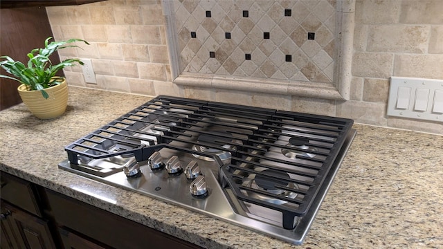 details featuring light stone counters, tasteful backsplash, stainless steel gas stovetop, and dark brown cabinets