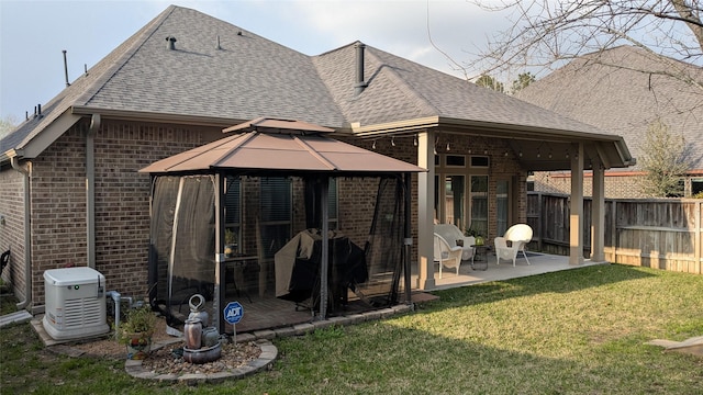 back of house featuring brick siding, a gazebo, roof with shingles, and fence