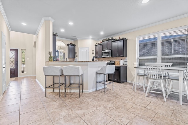 kitchen featuring light tile patterned floors, a kitchen breakfast bar, ornamental molding, decorative backsplash, and stainless steel microwave