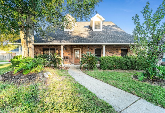 view of front of property featuring a front yard, brick siding, and roof with shingles