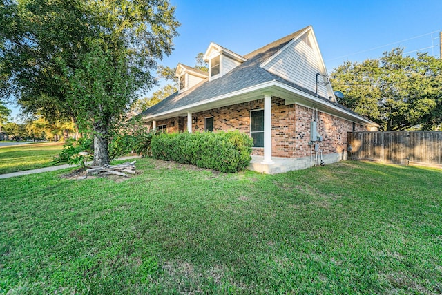 view of side of property featuring a yard, fence, and brick siding