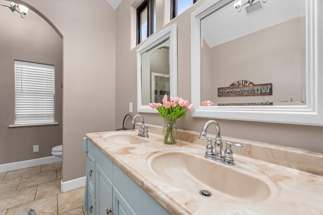 bathroom featuring toilet, double vanity, baseboards, and a sink