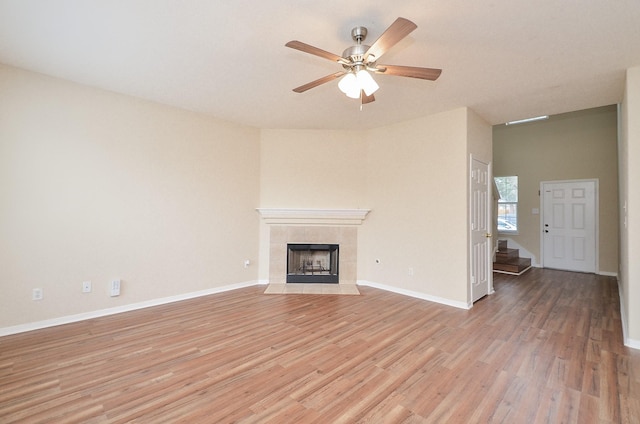 unfurnished living room with baseboards, a fireplace, a ceiling fan, and light wood-style floors