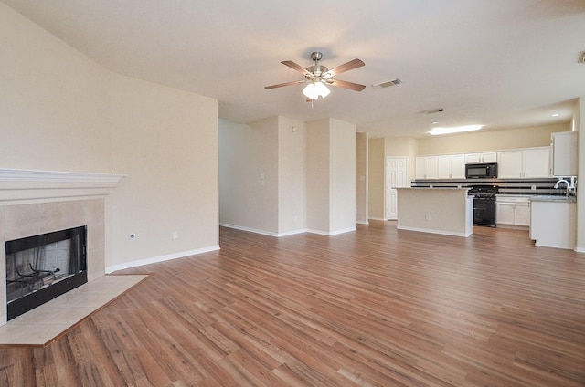 unfurnished living room with light wood finished floors, visible vents, a ceiling fan, a tiled fireplace, and a sink