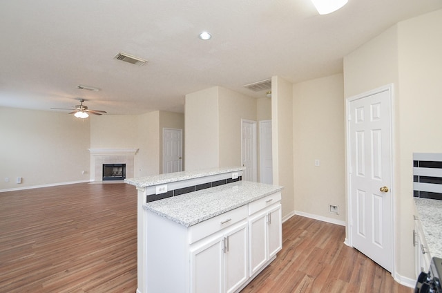 kitchen featuring a fireplace, visible vents, white cabinets, a center island, and light wood finished floors