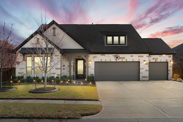 view of front of home with an attached garage, a shingled roof, concrete driveway, stone siding, and a lawn