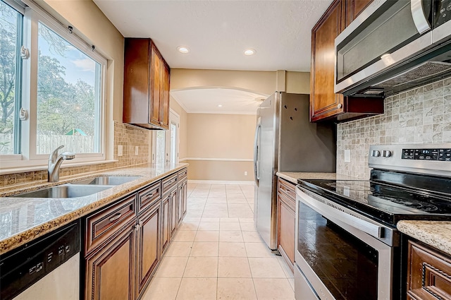 kitchen featuring light tile patterned floors, arched walkways, stainless steel appliances, a sink, and light stone countertops