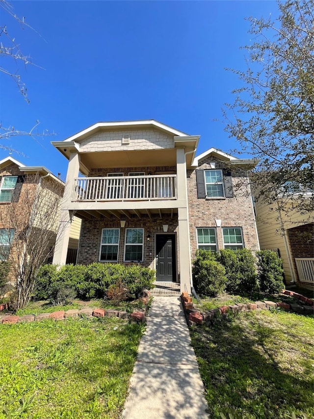 view of front of home with a balcony, a front yard, and brick siding