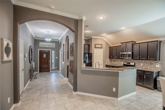 kitchen with light stone countertops, arched walkways, dark brown cabinets, appliances with stainless steel finishes, and tasteful backsplash