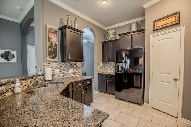 kitchen with stone counters, a sink, dark brown cabinets, crown molding, and black fridge