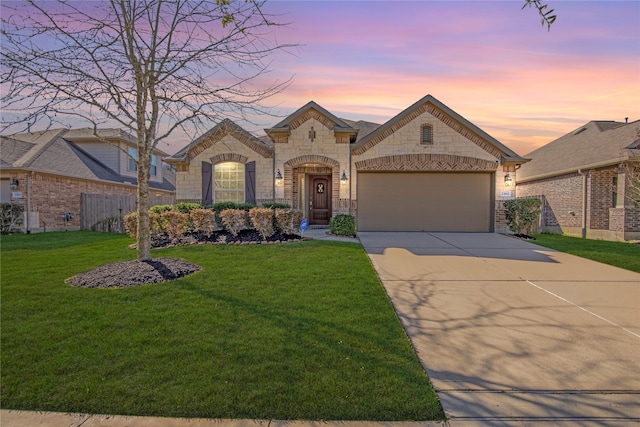 french country inspired facade featuring stone siding, a yard, a garage, and driveway