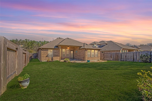 back of house at dusk with a yard, brick siding, roof with shingles, and a fenced backyard