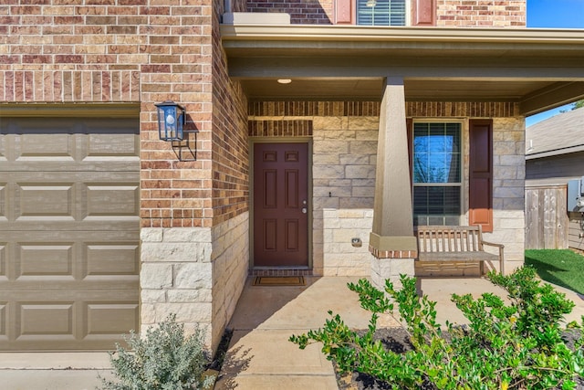 property entrance featuring an attached garage, covered porch, stone siding, and brick siding