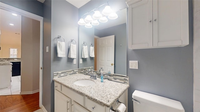 half bathroom with decorative backsplash, toilet, vanity, wood finished floors, and baseboards