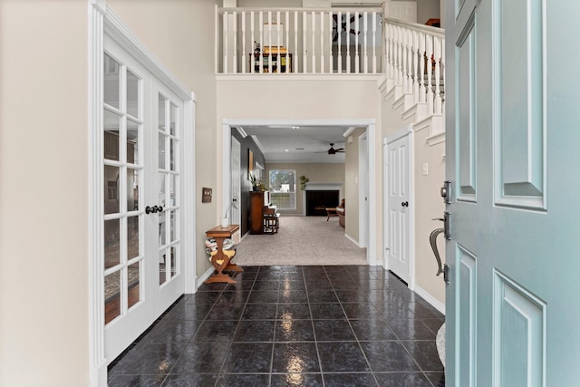 carpeted entryway with french doors, a fireplace, a towering ceiling, tile patterned flooring, and baseboards