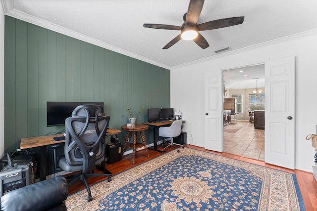 office area featuring baseboards, visible vents, wood finished floors, crown molding, and ceiling fan with notable chandelier