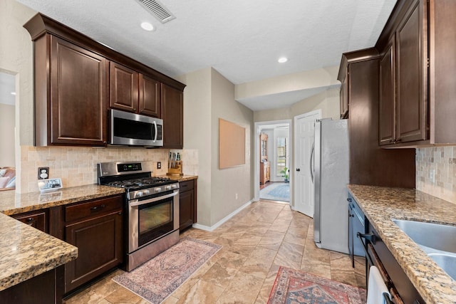 kitchen featuring light stone counters, stainless steel appliances, decorative backsplash, dark brown cabinetry, and baseboards