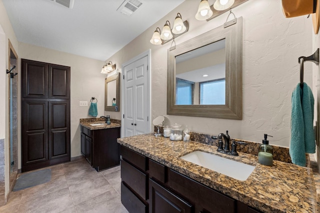 full bathroom with a textured wall, two vanities, a sink, and visible vents