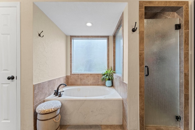 bathroom featuring a textured wall, a stall shower, and a bath