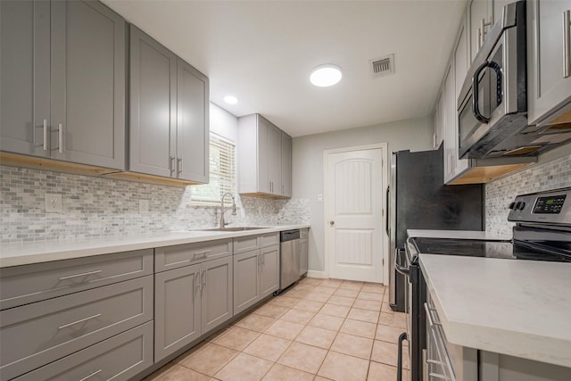 kitchen featuring light tile patterned floors, visible vents, stainless steel appliances, gray cabinetry, and a sink