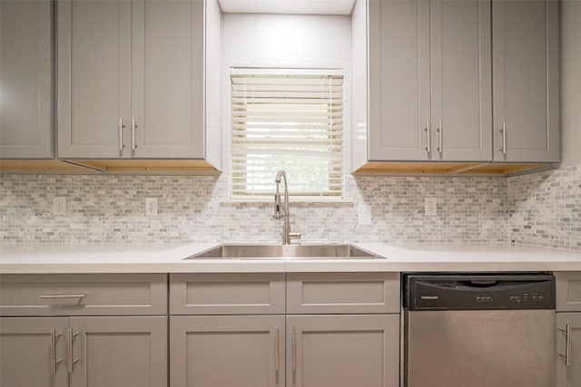 kitchen with gray cabinets, light countertops, decorative backsplash, a sink, and dishwasher