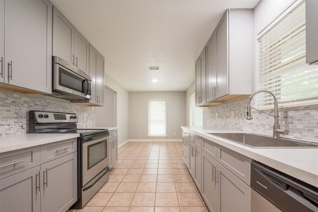 kitchen featuring light tile patterned floors, stainless steel appliances, gray cabinets, visible vents, and a sink