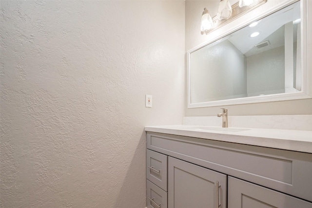 bathroom featuring visible vents, a textured wall, and vanity