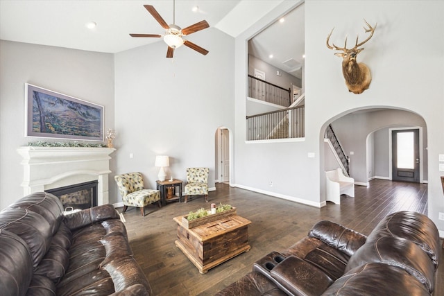 living area with arched walkways, stairway, wood finished floors, a fireplace, and high vaulted ceiling