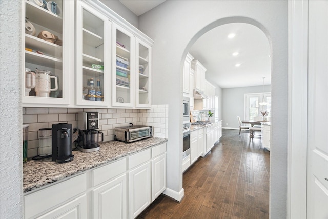 kitchen with arched walkways, white cabinets, dark wood finished floors, glass insert cabinets, and appliances with stainless steel finishes