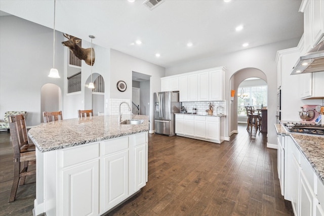 kitchen featuring tasteful backsplash, arched walkways, dark wood finished floors, range with gas cooktop, and stainless steel fridge with ice dispenser