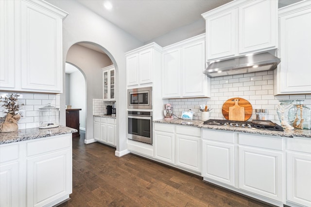 kitchen featuring stainless steel appliances, dark wood-style flooring, white cabinets, range hood, and light stone countertops